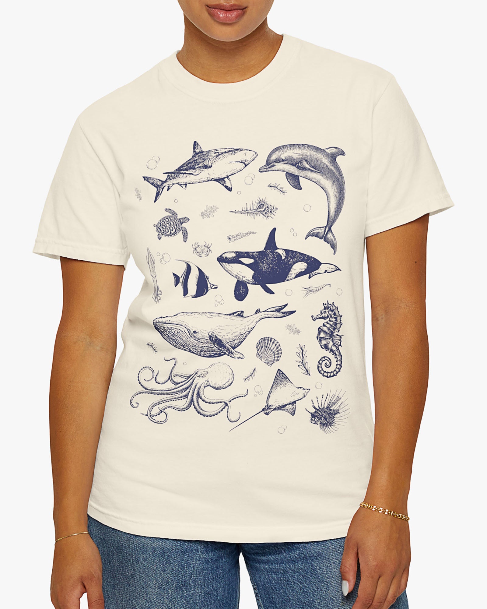 Woman wearing a natural shirt featuring a vintage 90s sea creatures collage graphic with whales, dolphins, turtles, and ocean life, perfect for retro nature lovers