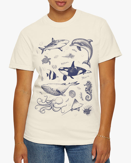 Woman wearing a natural shirt featuring a vintage 90s sea creatures collage graphic with whales, dolphins, turtles, and ocean life, perfect for retro nature lovers