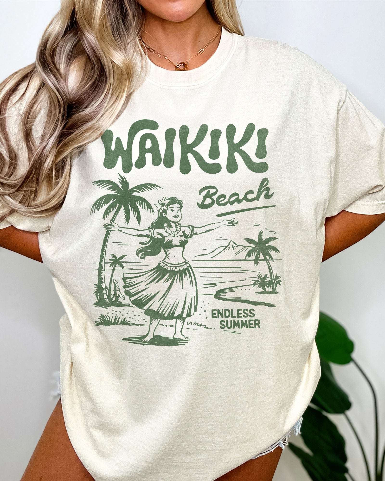 Woman wearing an ivory "Waikiki Beach – Endless Summer" shirt with a retro graphic of a Hawaiian beach and a girl.