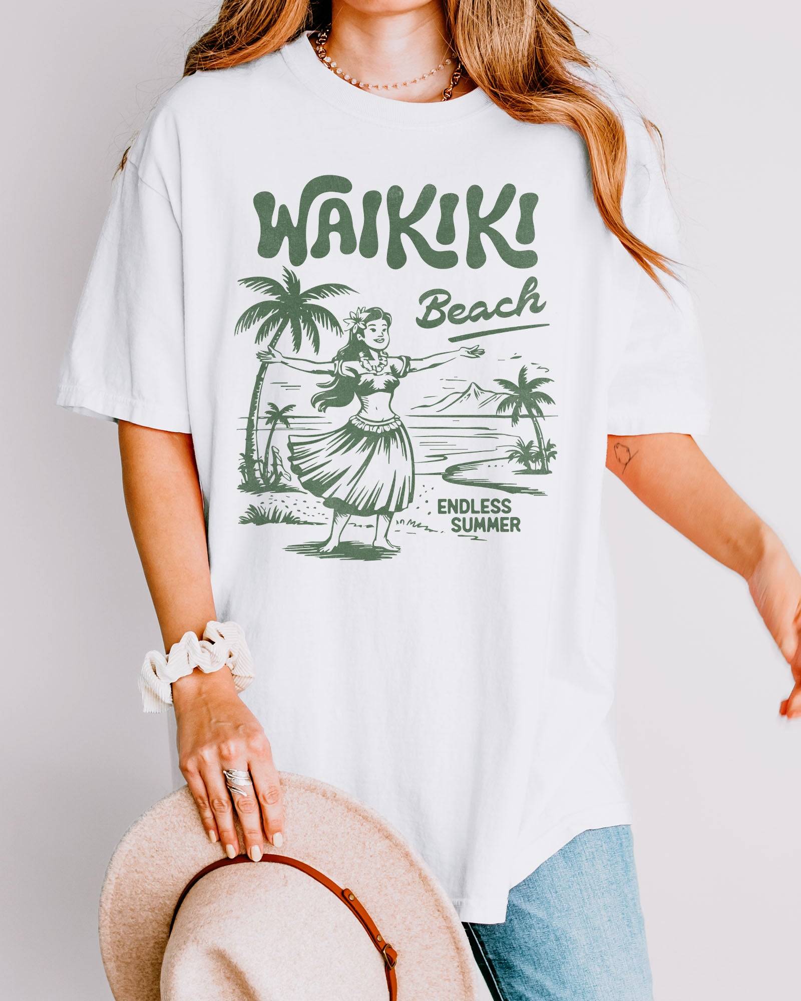 Woman wearing a white "Waikiki Beach – Endless Summer" shirt with a retro graphic of a Hawaiian beach and a girl.