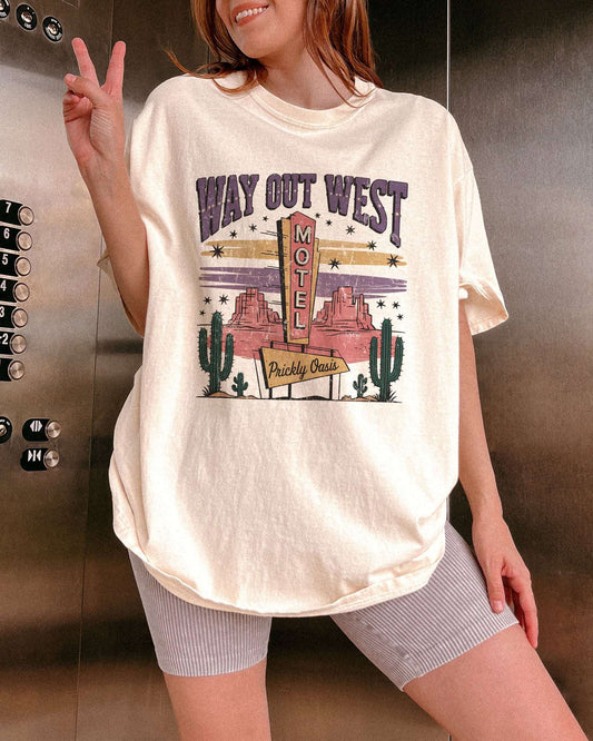 Model wearing ivory color shirt with 'Way Out West Motel' western desert graphic design