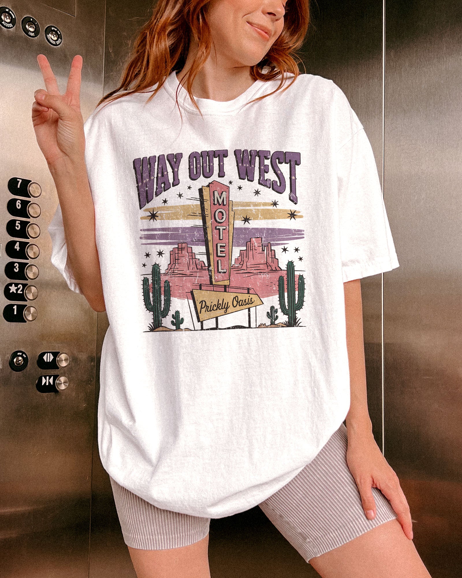 Woman wearing white color shirt with 'Way Out West Motel' western desert graphic design