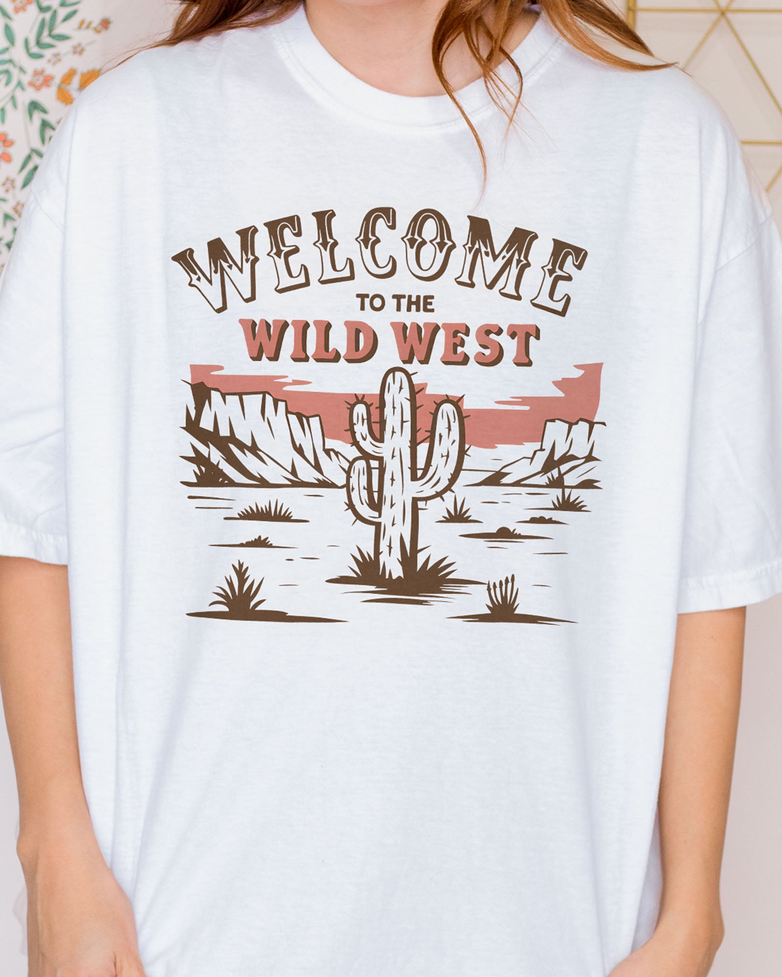 Close-up of woman wearing an ivory 'Welcome To The Wild West' shirt with a retro western graphic of a desert and cactus.