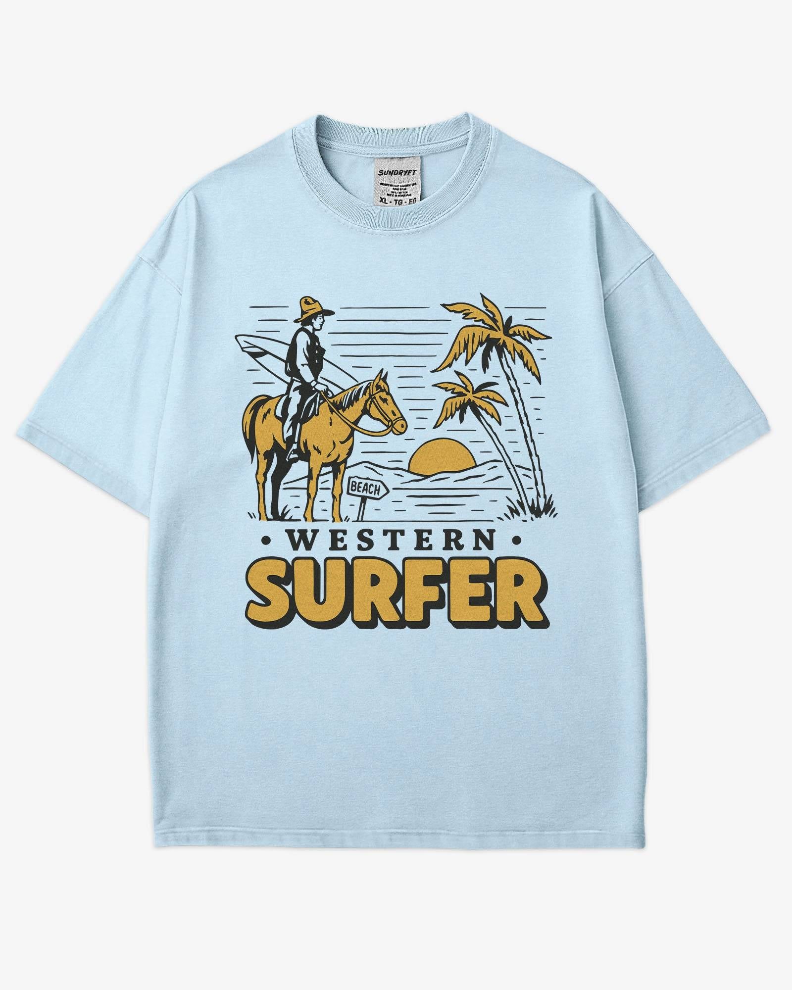 Flat lay chambray 'Western Surfer' shirt with a retro graphic of a cowboy on a horse in a desert, following a beach signpost.
