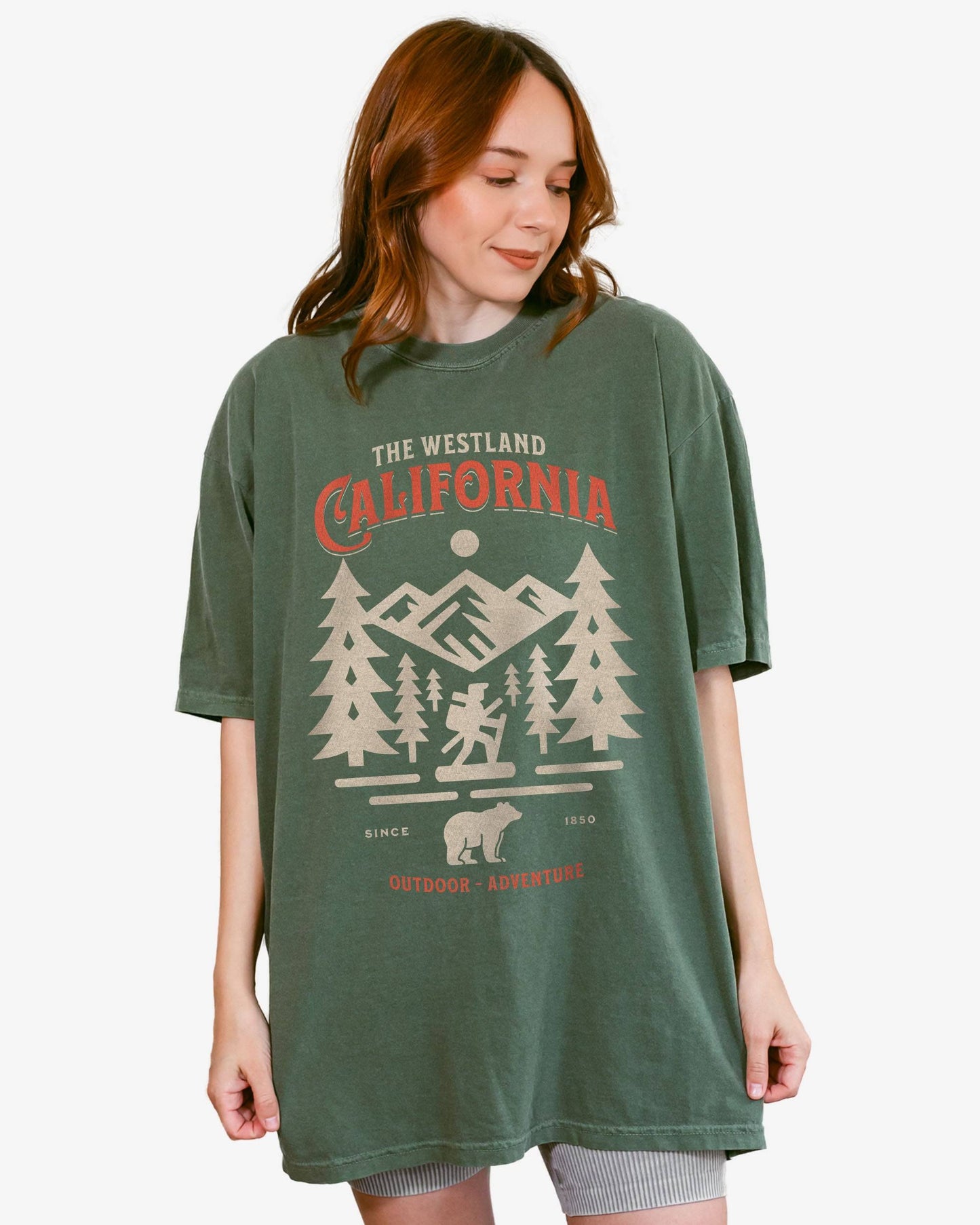 Woman wearing a moss Westland California Outdoor Adventure shirt with a retro vector graphic of a hiker, bear, and mountains.