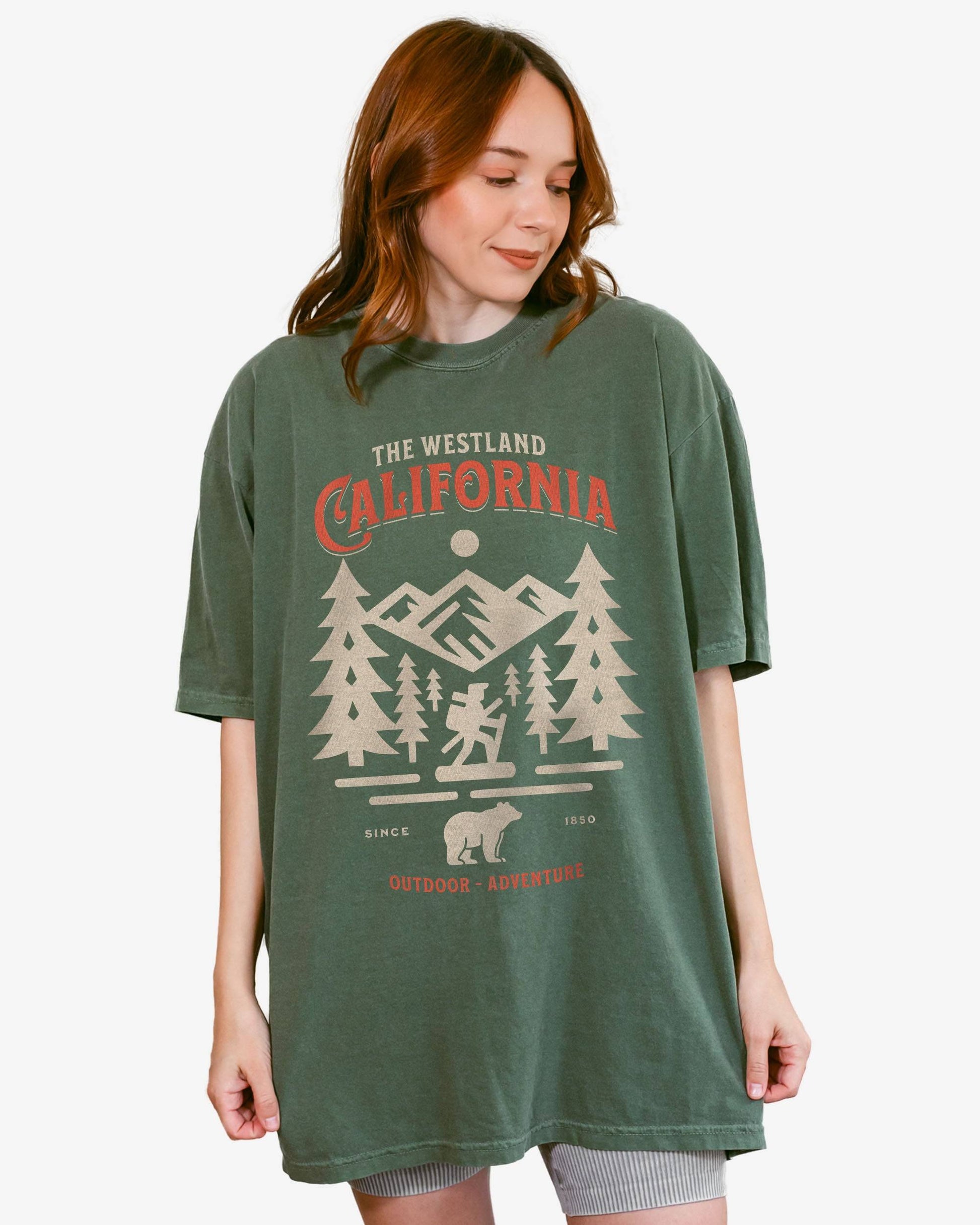 Woman wearing a moss Westland California Outdoor Adventure shirt with a retro vector graphic of a hiker, bear, and mountains.