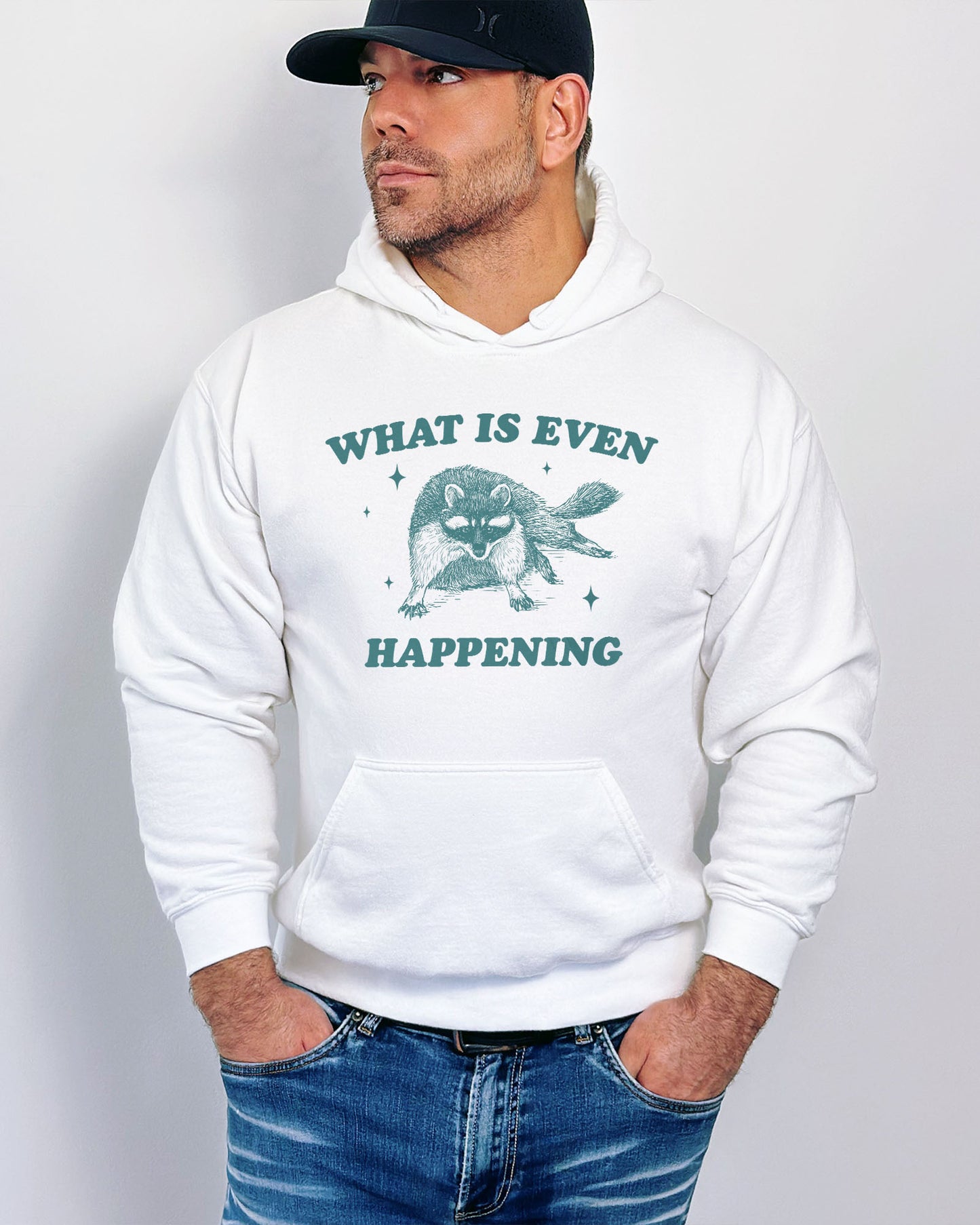 Man wearing a white 'What Is Even Happening' hoodie featuring a funny retro raccoon graphic.