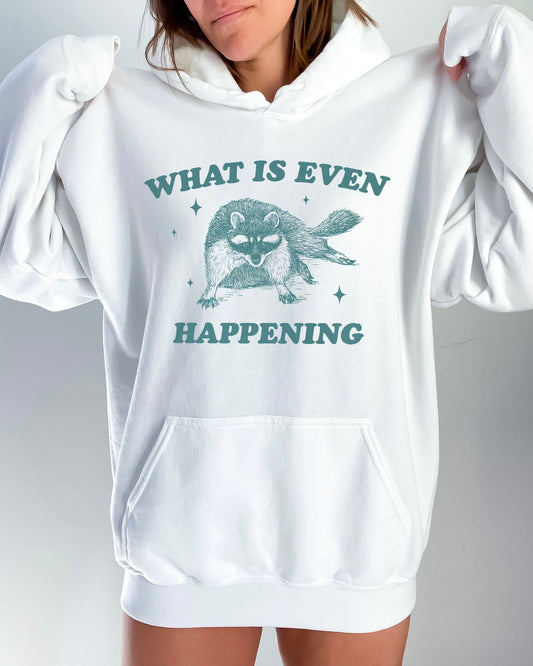 Woman wearing a white-colored 'What Is Even Happening' hoodie featuring a funny retro raccoon graphic.