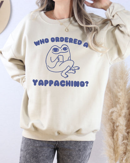 Model wearing sand color sweatshirt with 'Who Ordered A Yappachino' graphic design