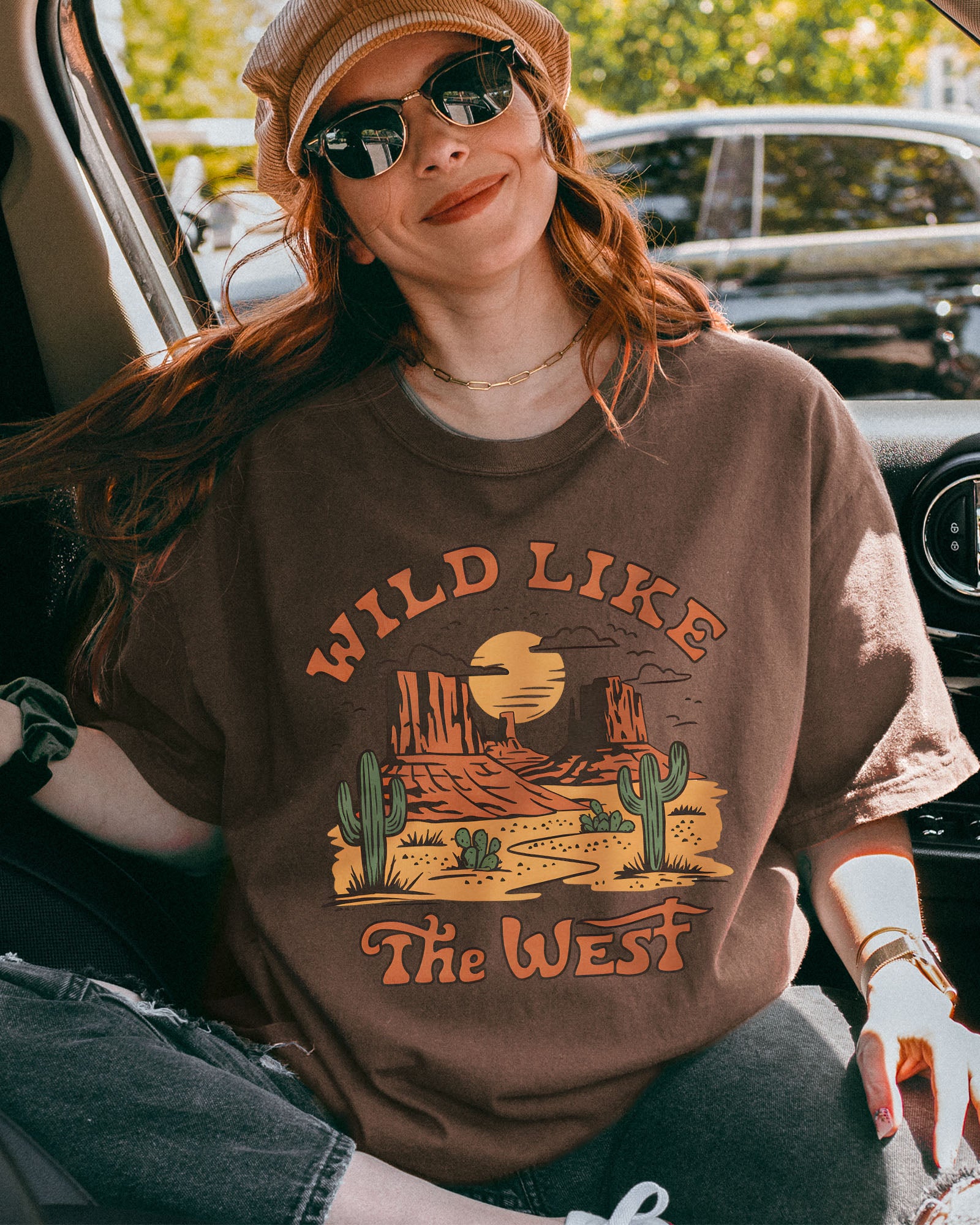 Woman wearing an espresso-colored "Wild Like the West" shirt with a retro graphic of a western desert.