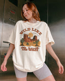 Woman wearing an ivory "Wild Like the West" shirt with a retro graphic of a western desert.