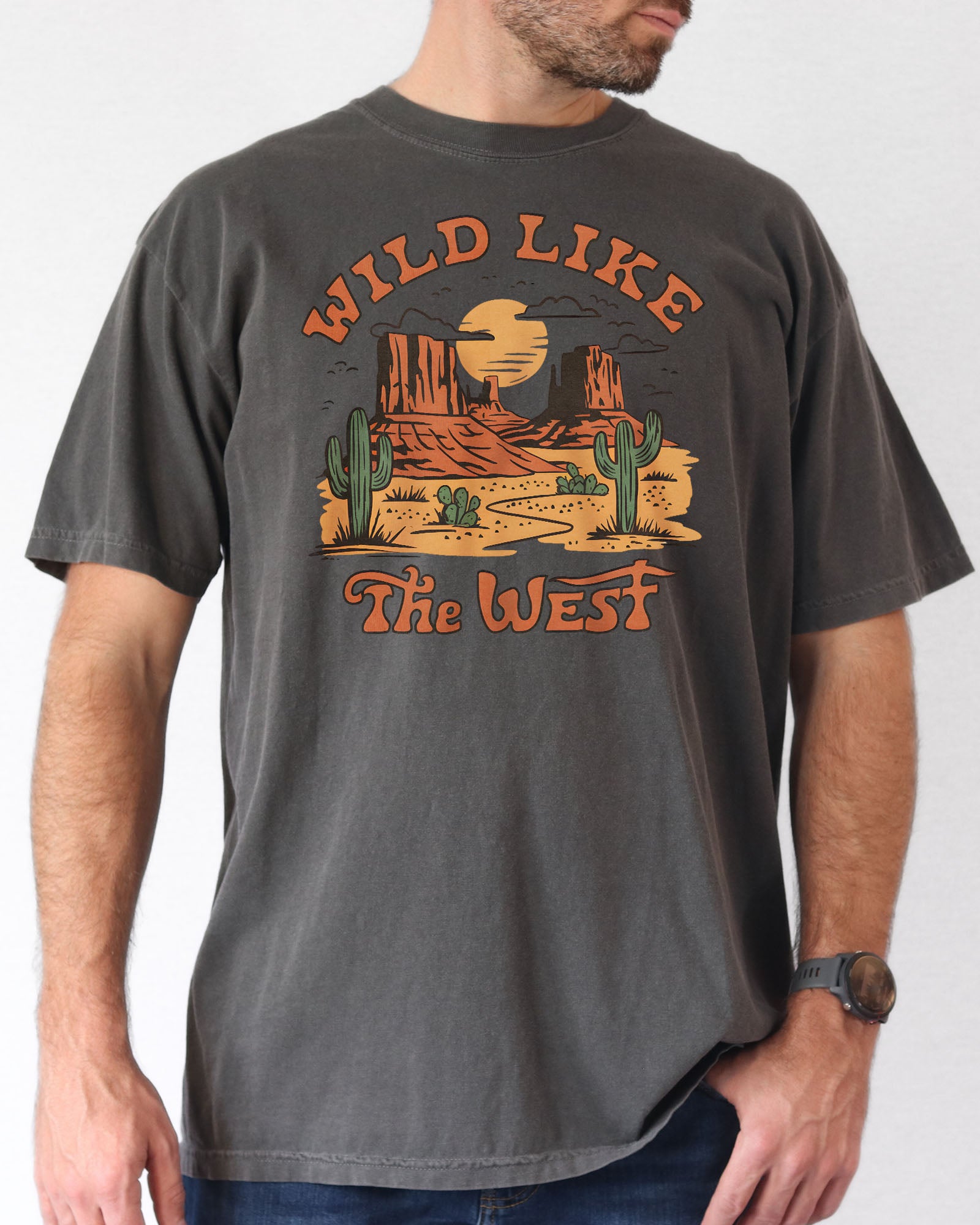 Man wearing a pepper-colored "Wild Like the West" shirt with a retro graphic of a western desert.