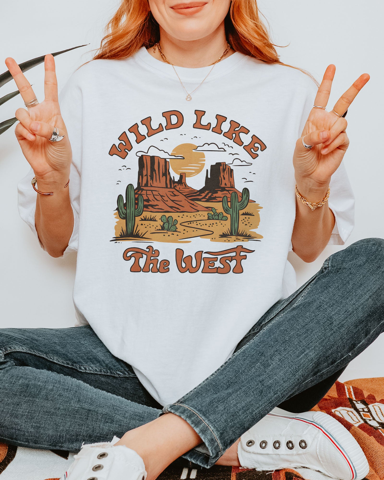 Woman wearing a white "Wild Like the West" shirt with a retro graphic of a western desert.