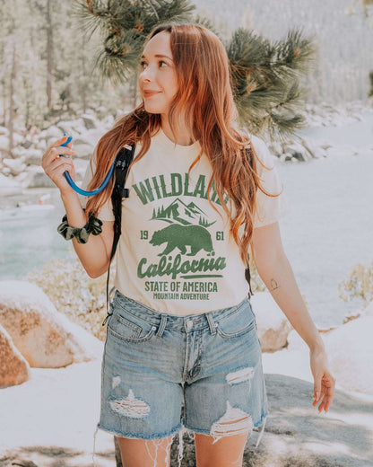 Woman wearing an ivory Wildland California shirt with a retro graphic of a bear and mountains.