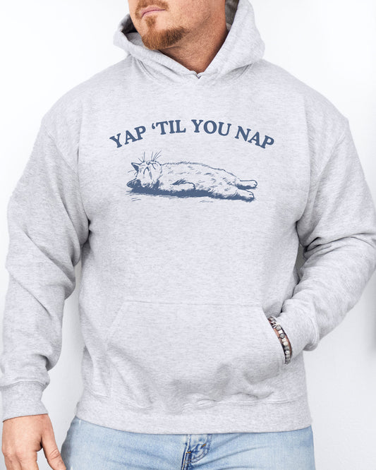 Man wearing an ash gray hoodie featuring a funny retro sleeping cat graphic and the quote 'Yap 'Til You Nap'.