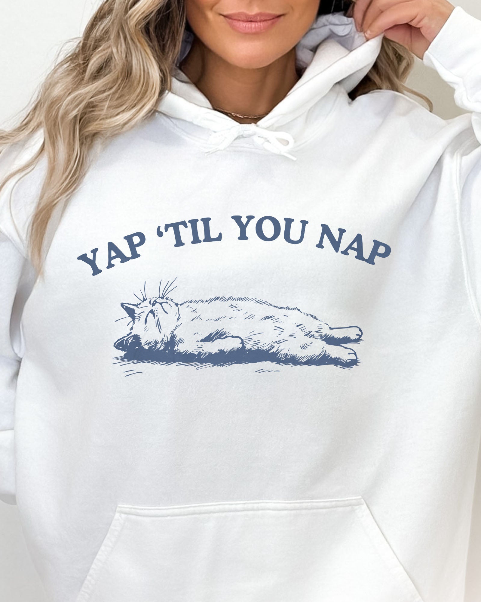 Close-up of a white hoodie featuring a funny retro sleeping cat graphic and the quote 'Yap 'Til You Nap'.
