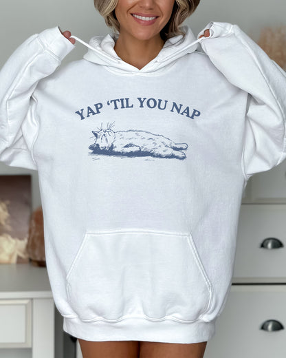 Woman wearing a white hoodie featuring a funny retro sleeping cat graphic and the quote 'Yap 'Til You Nap'.
