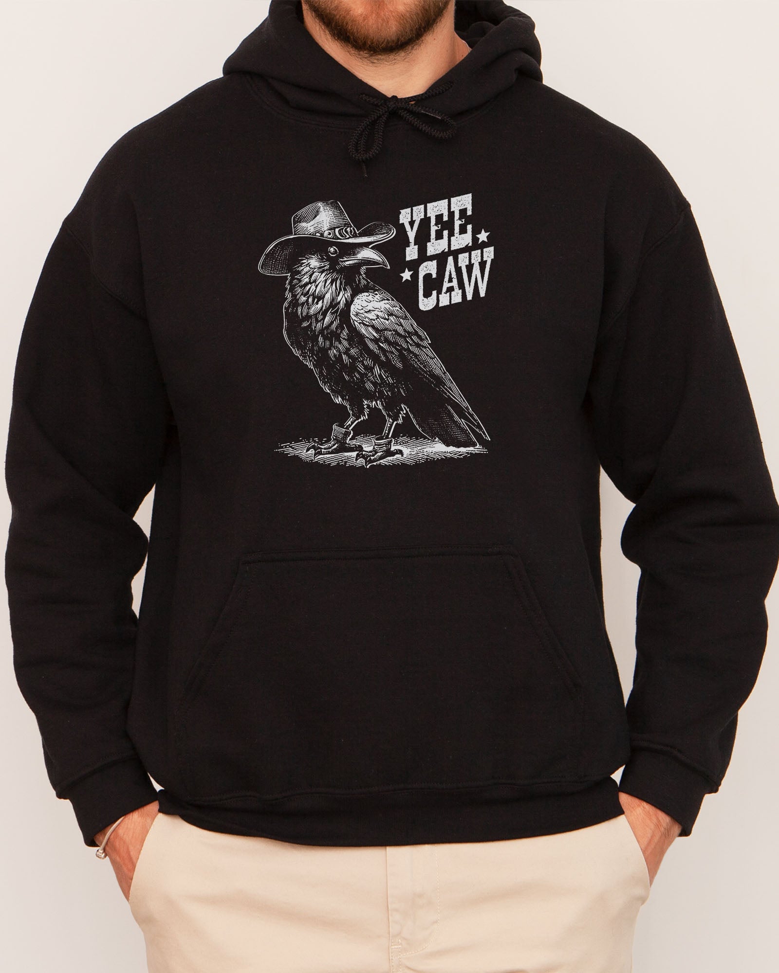 Man wearing a black-colored hoodie featuring a funny retro cowboy crow graphic and the quote 'Yee Caw'.