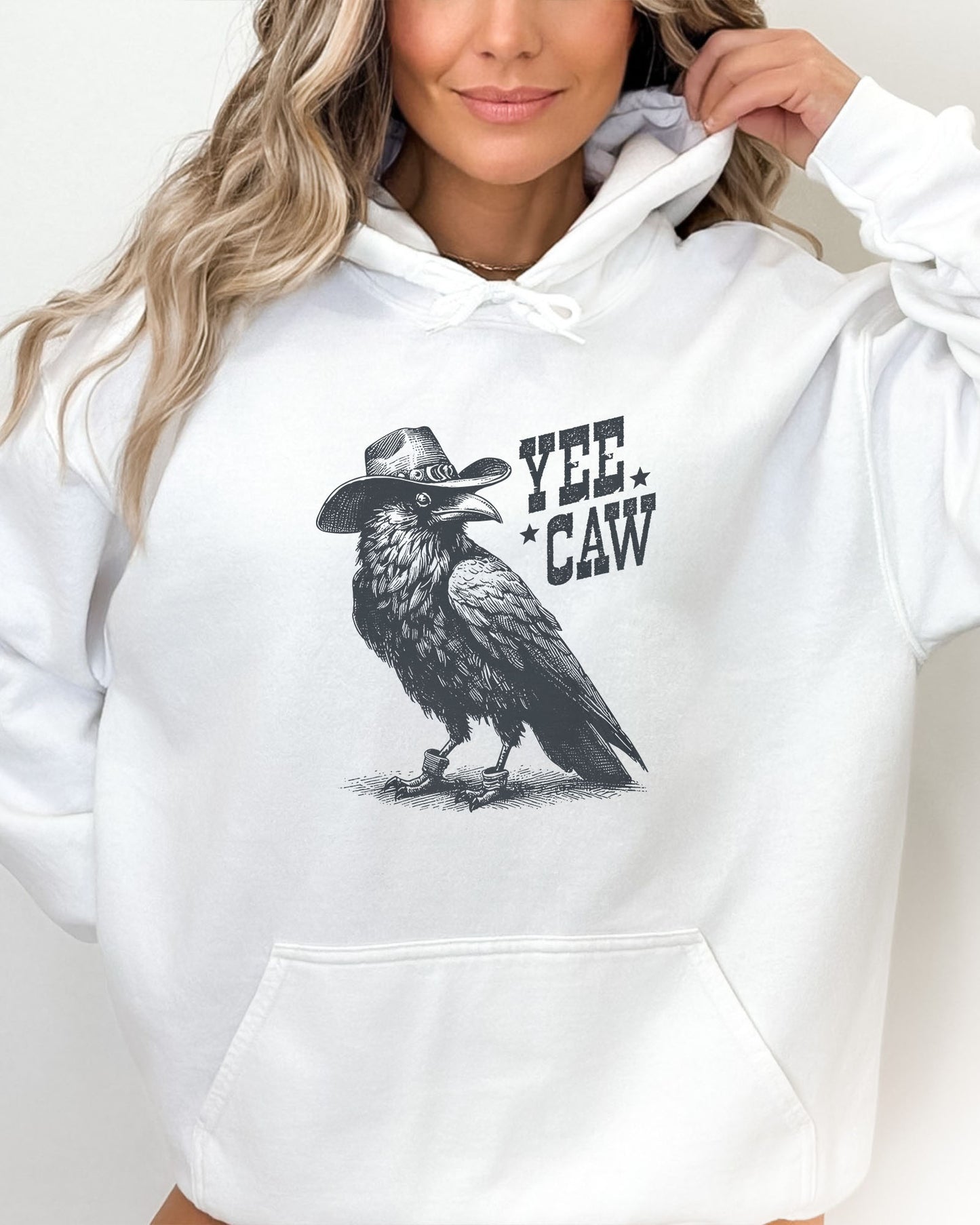 Woman wearing a white-colored hoodie featuring a funny retro cowboy crow graphic and the quote 'Yee Caw'.