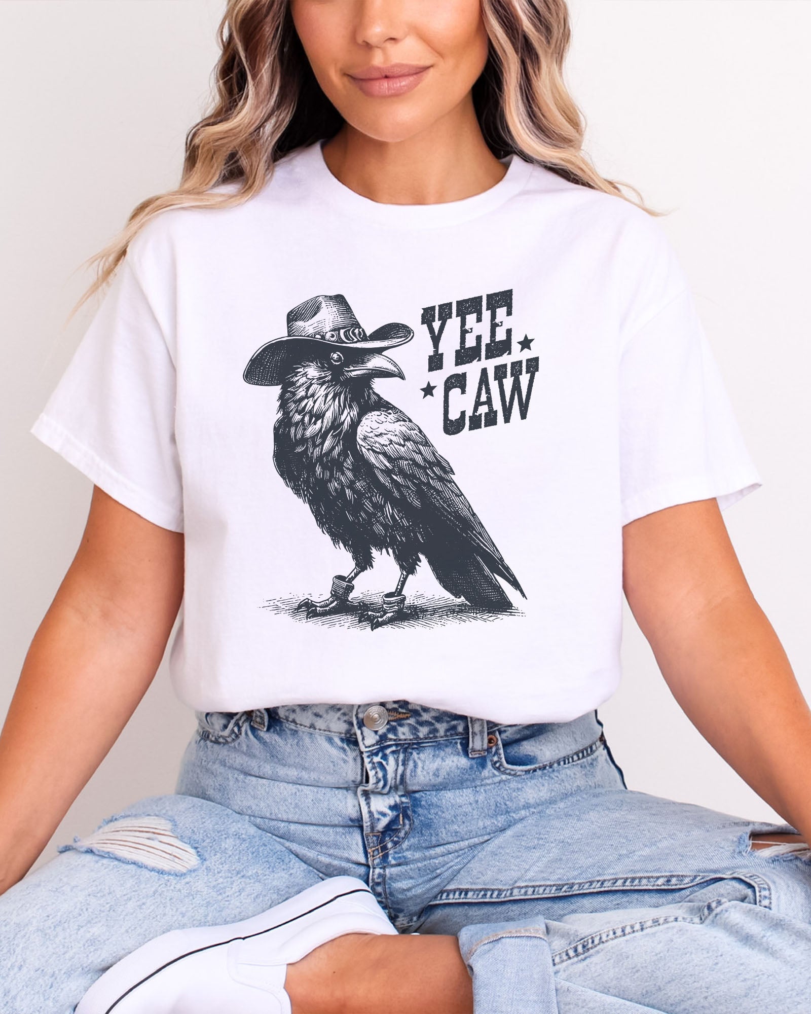 Woman wearing white-colored 'Yee Caw' shirt featuring a funny retro cowboy crow graphic.
