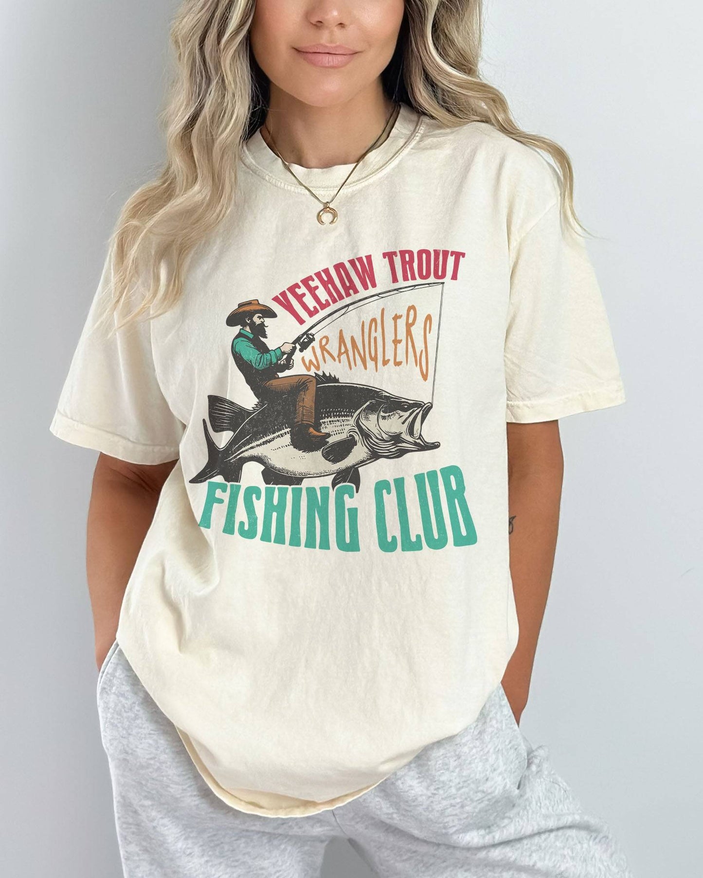 Model wearing ivory color shirt with 'Yeehaw Trout Wranglers Fishing Club' graphic design