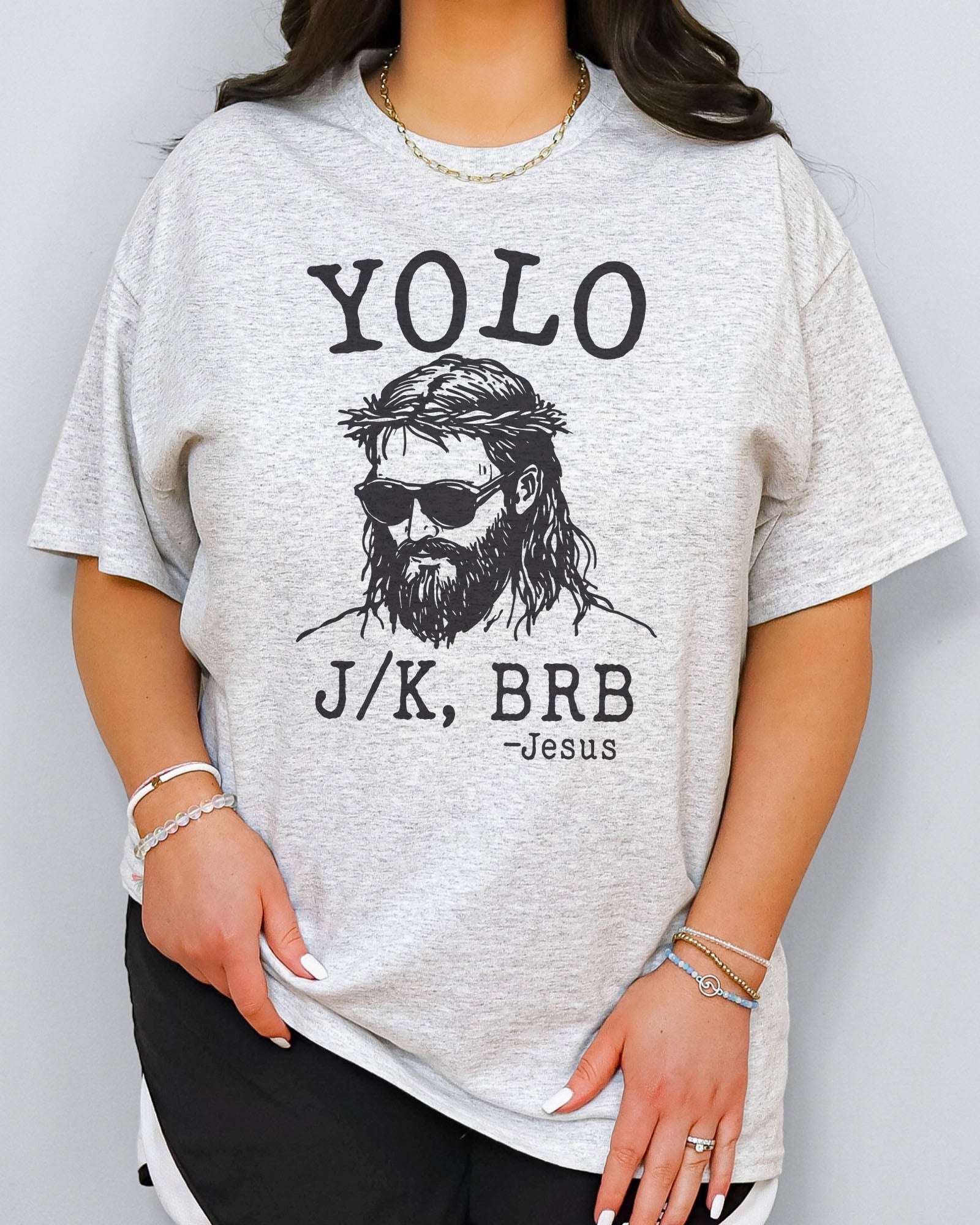 Model wearing ash color shirt with 'YOLO J/K BRB Jesus' graphic design