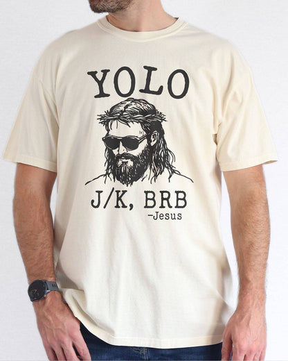 Model wearing natural color shirt with 'YOLO J/K BRB Jesus' graphic design