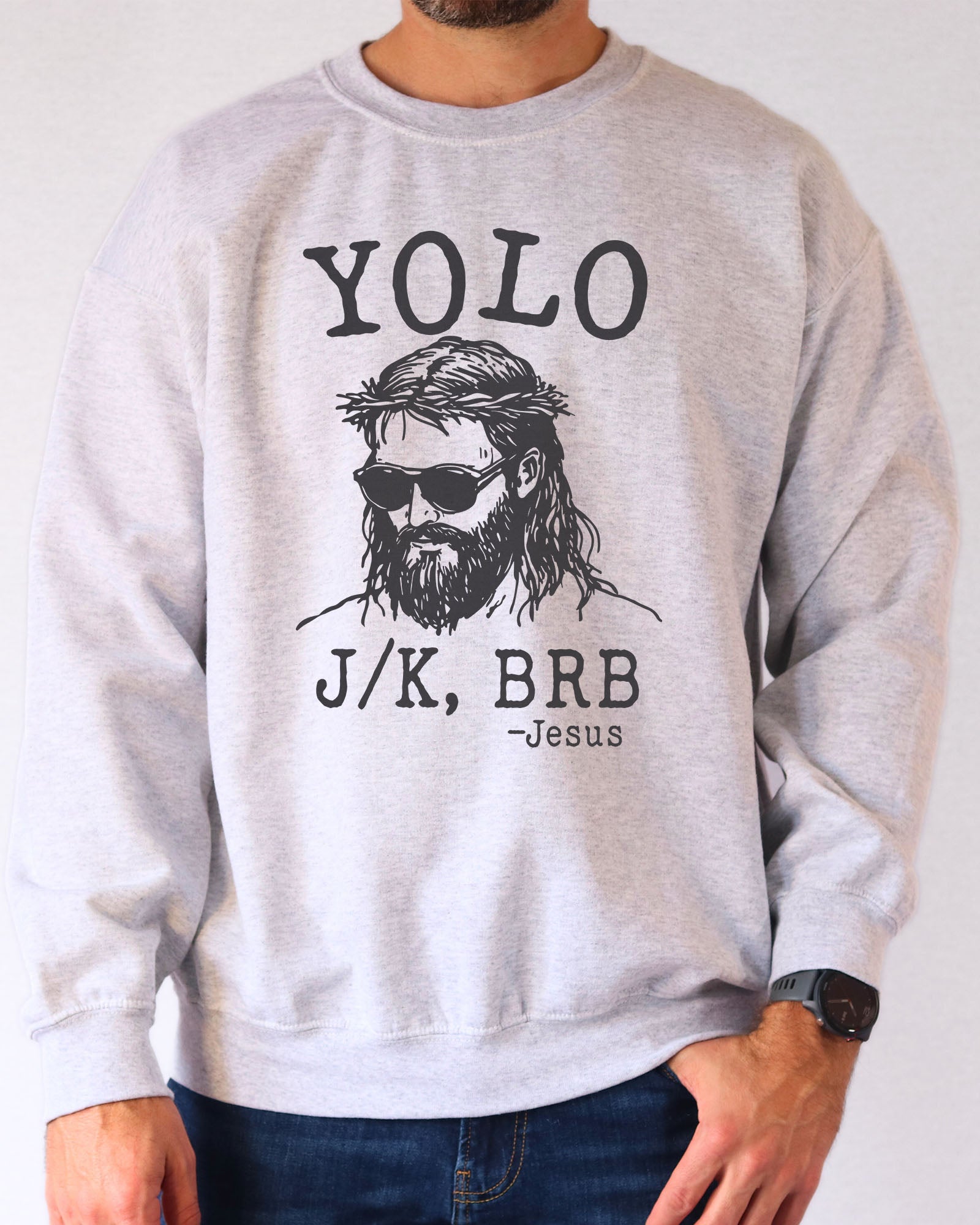 Model wearing ash color sweatshirt with 'YOLO Jesus J/K BRB' graphic design