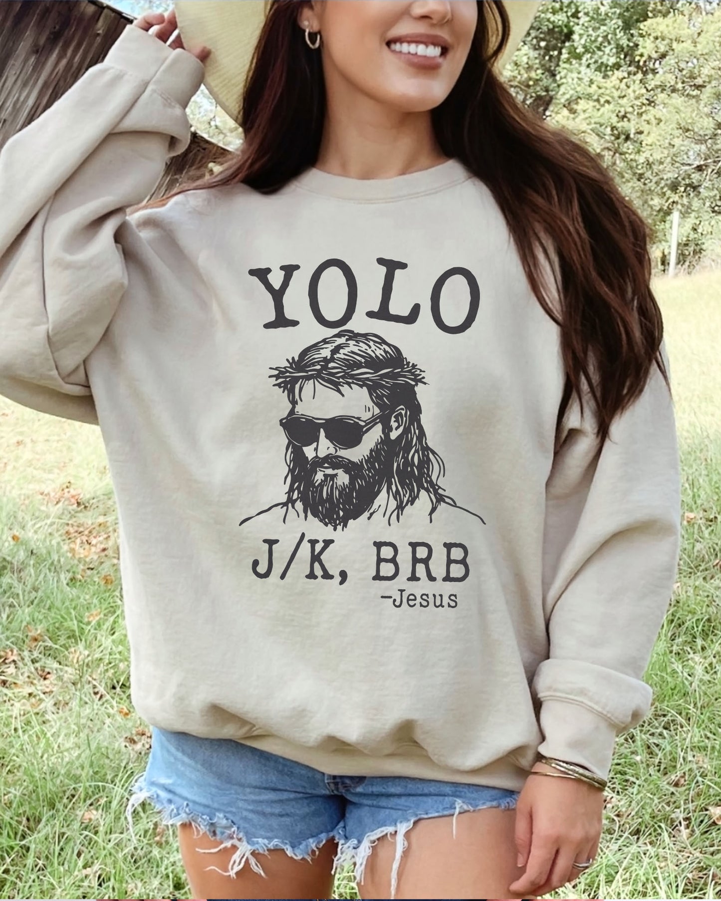 Model wearing sand color sweatshirt with 'YOLO Jesus J/K BRB' graphic design