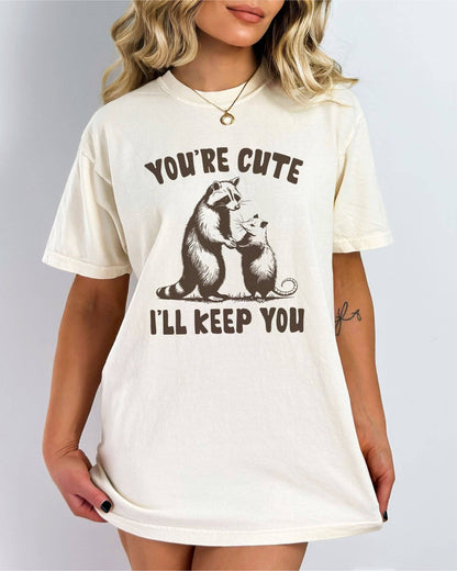 Model wearing ivory color shirt with 'You're Cute I'll Keep You' graphic design