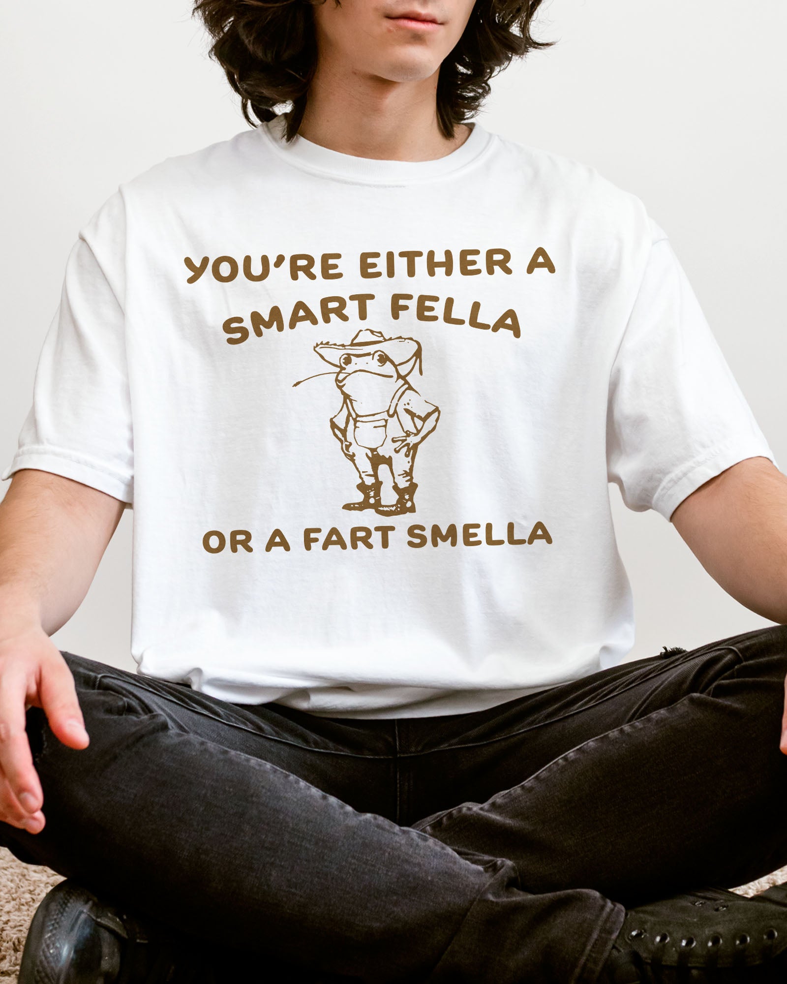 Man wearing a white "You’re Either a Smart Fella or a Fart Smella" shirt with a funny retro outline graphic of a cowboy frog.
