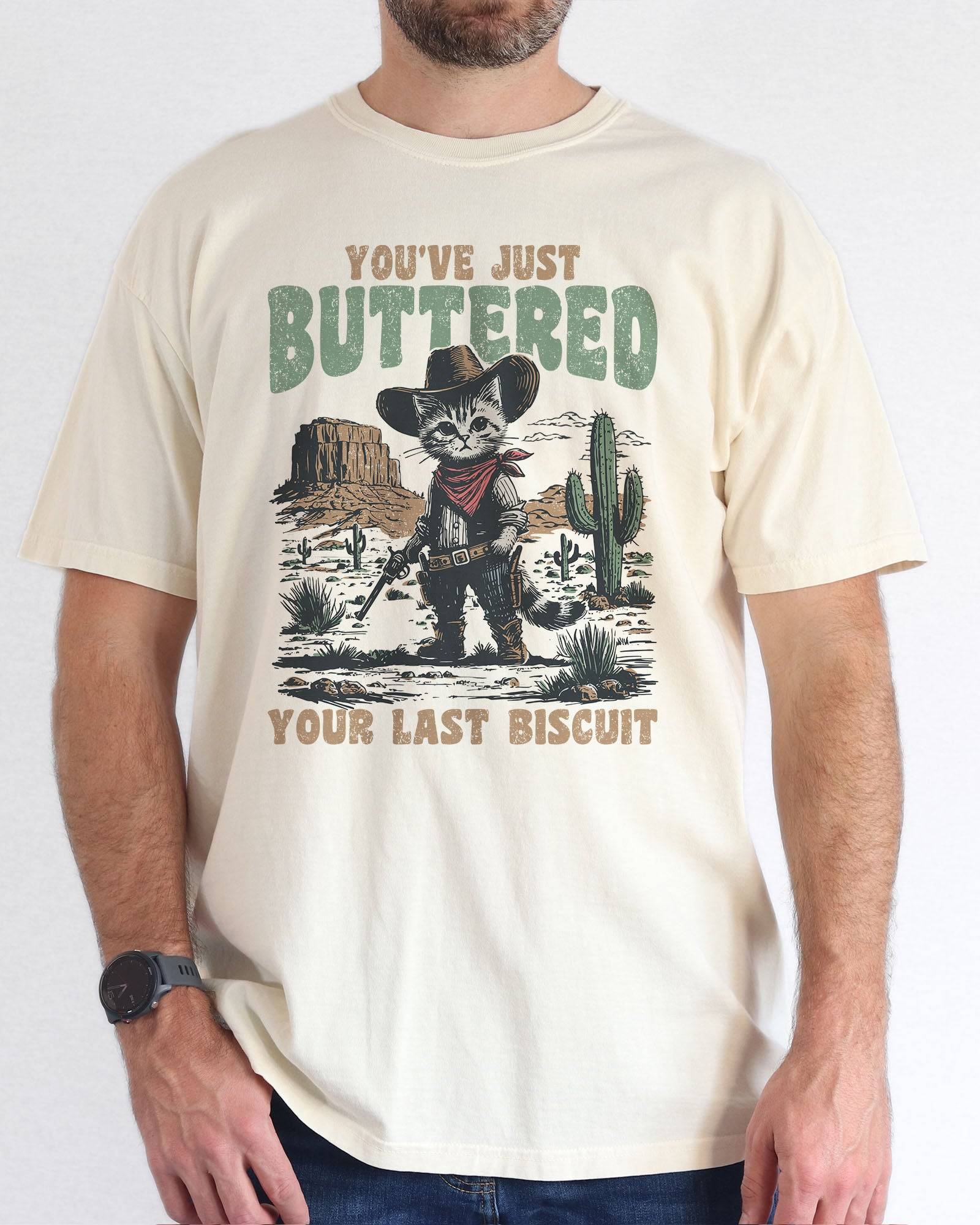 Model wearing natural color shirt with 'You've Just Buttered Your Last Biscuit' cowboy kitten graphic design