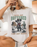Model wearing white color shirt with 'You've Just Buttered Your Last Biscuit' cowboy kitten graphic design
