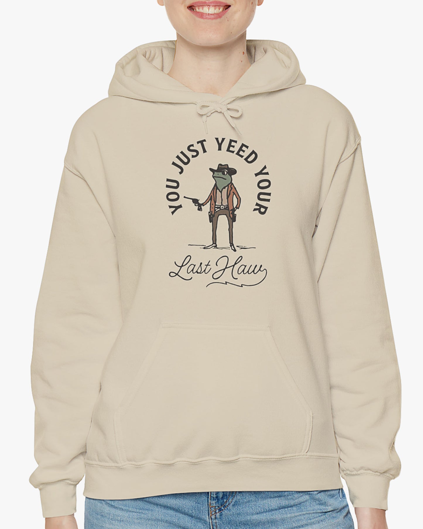 Woman wearing sand beige 'You Just Yeed Your Last Haw' hoodie with funny retro cowboy frog graphic