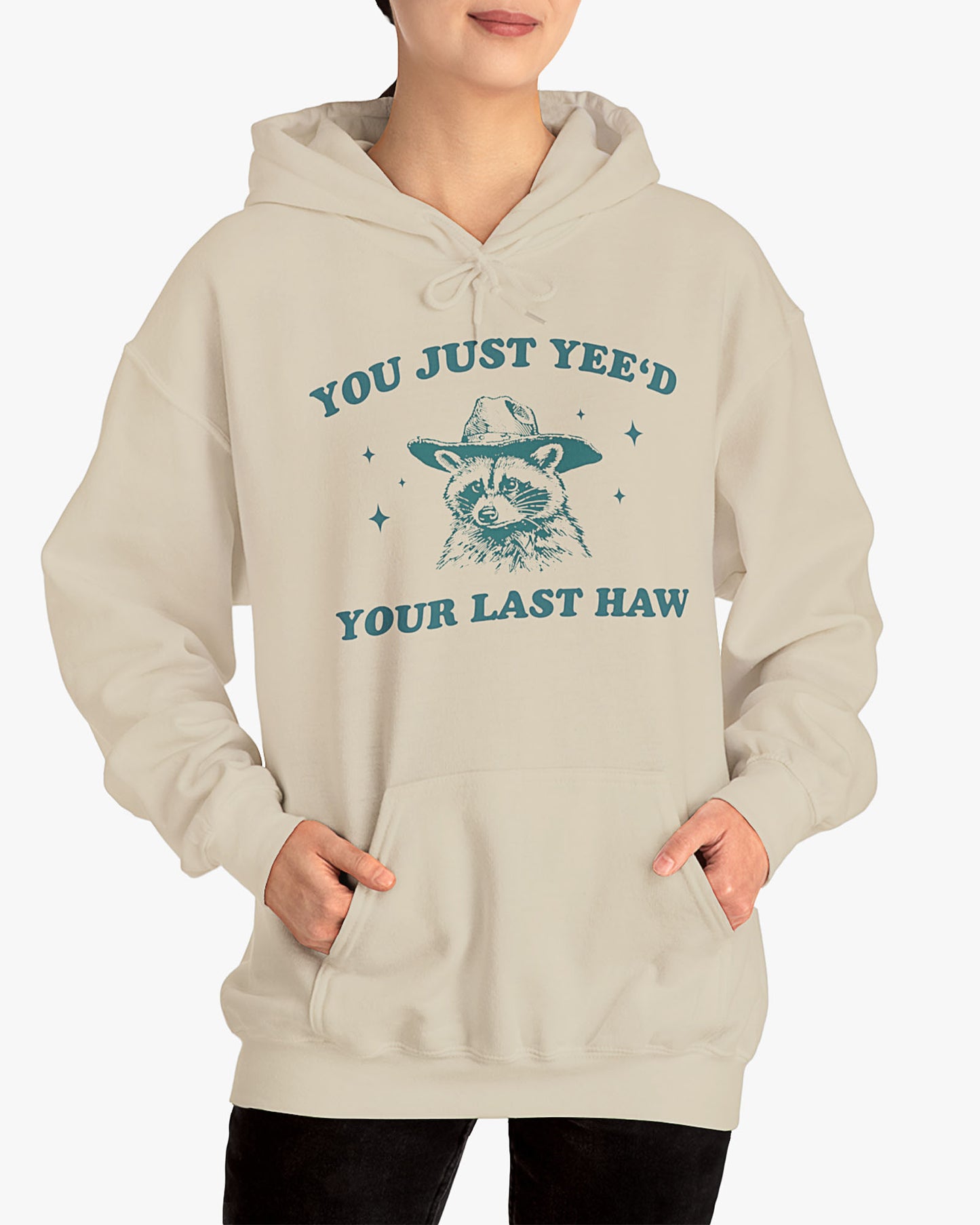 Woman wearing sand beige 'You Just Yeed Your Last Haw' hoodie with funny cowboy raccoon graphic