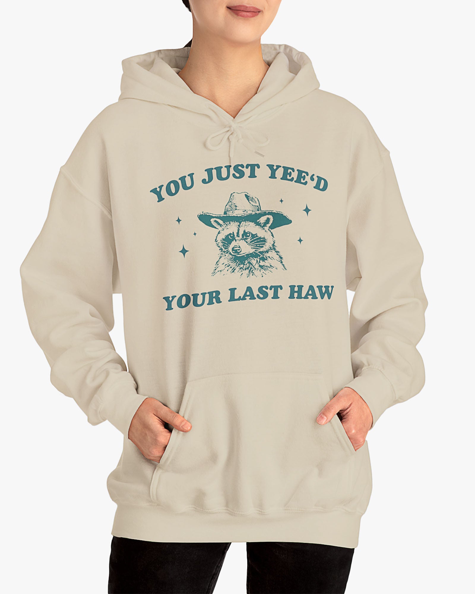 Woman wearing sand beige 'You Just Yeed Your Last Haw' hoodie with funny cowboy raccoon graphic