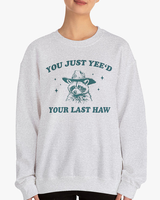 Woman wearing ash gray 'You Just Yeed Your Last Haw' sweatshirt with funny retro cowboy raccoon graphic
