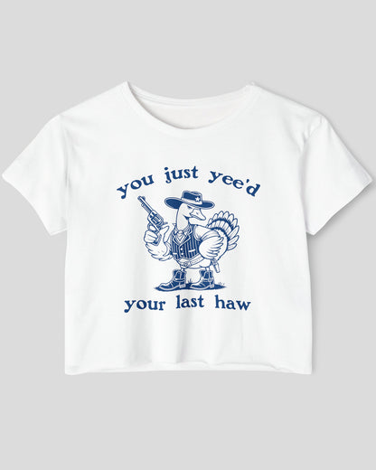 Flat lay of a white 'You Just Yee'd Your Last Haw' crop top featuring a funny retro cowboy goose graphic.