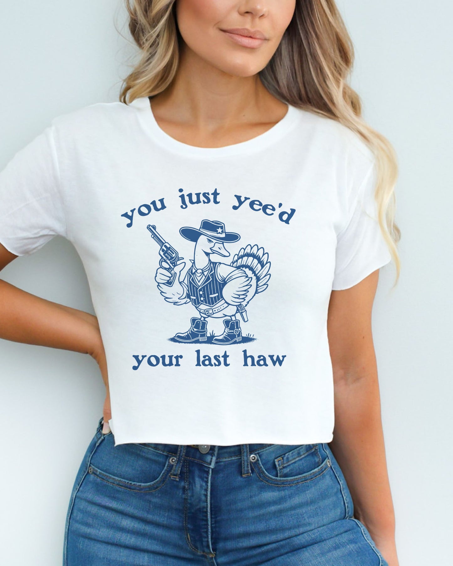 Woman wearing a white 'You Just Yee'd Your Last Haw' crop top featuring a funny retro cowboy goose graphic.