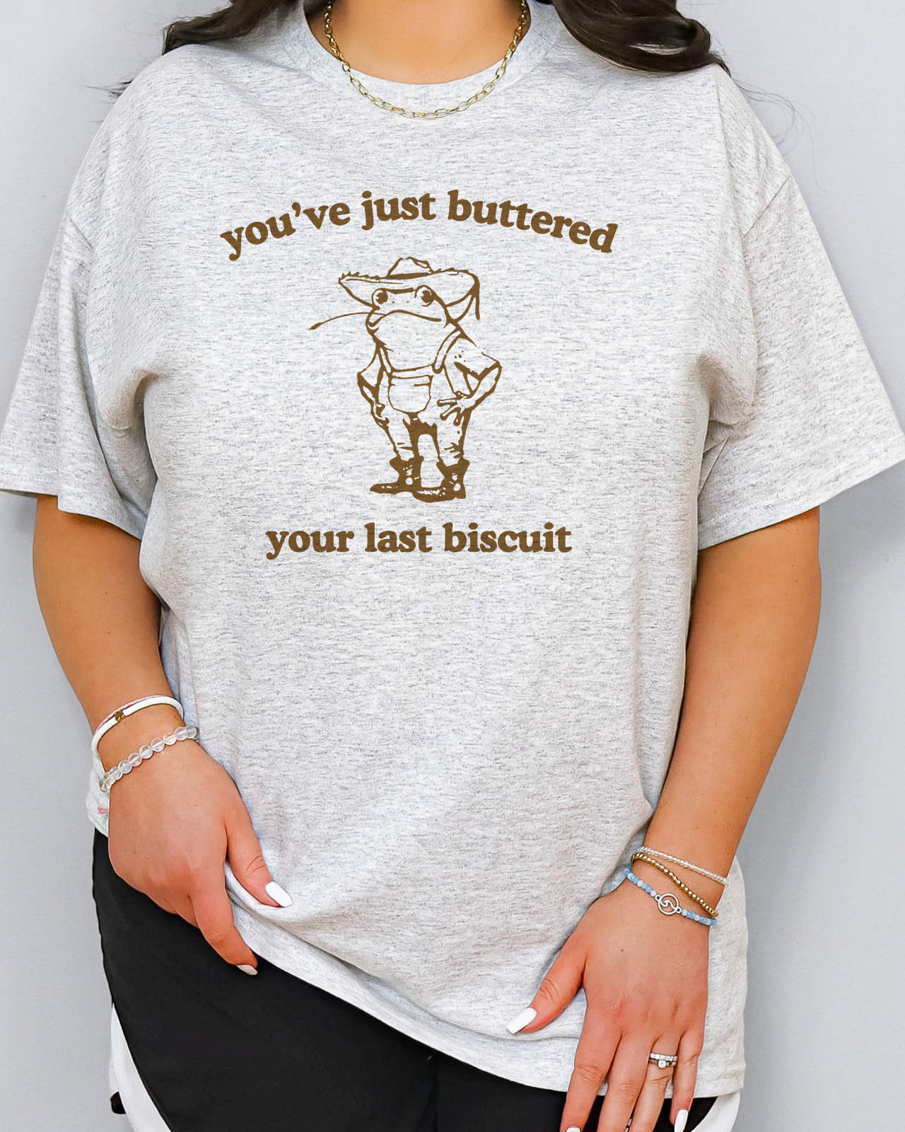 Woman wearing funny retro graphic shirt in ash grey color with the quote "You've Just Buttered Your Last Biscuit"