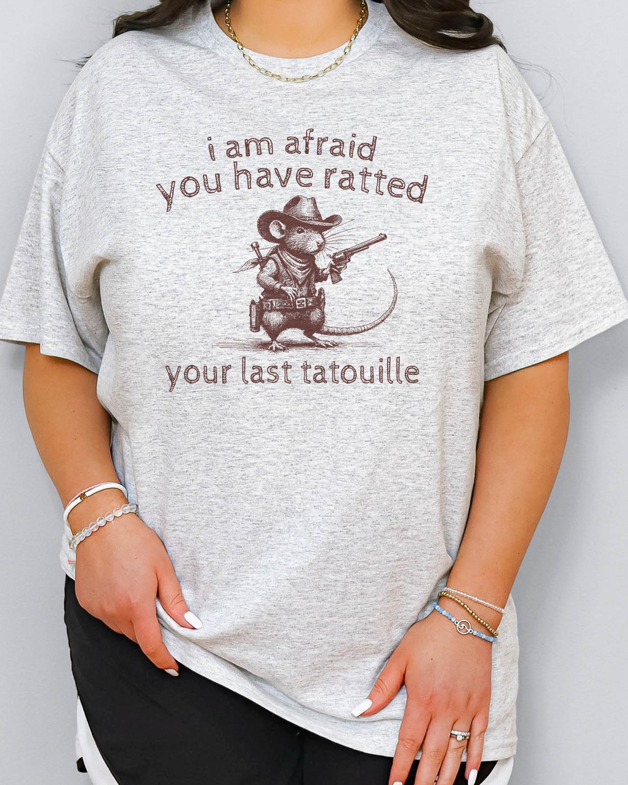 Woman wearing "You Have Ratted Your Last Tatouille" Shirt in ash grey color with a retro cowboy rat graphic