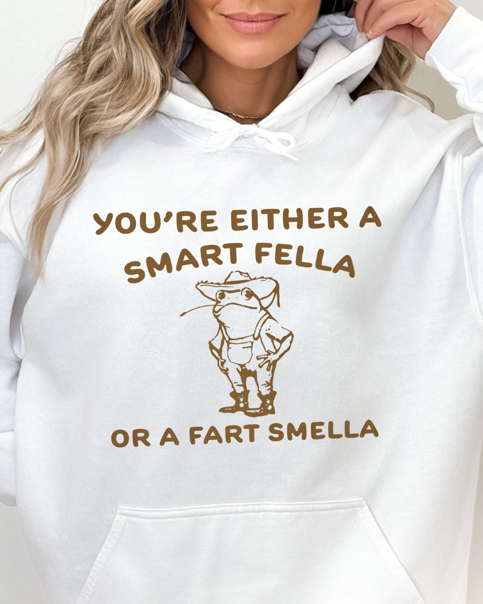 Close-up of a white hoodie featuring a funny retro-style country frog graphic with the quote 'You're Either A Smart Fella Or A Fart Smella'.