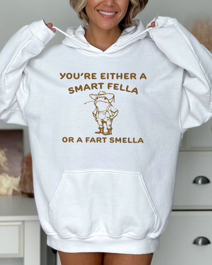 Woman wearing a white hoodie featuring a funny retro-style country frog graphic with the quote 'You're Either A Smart Fella Or A Fart Smella'.