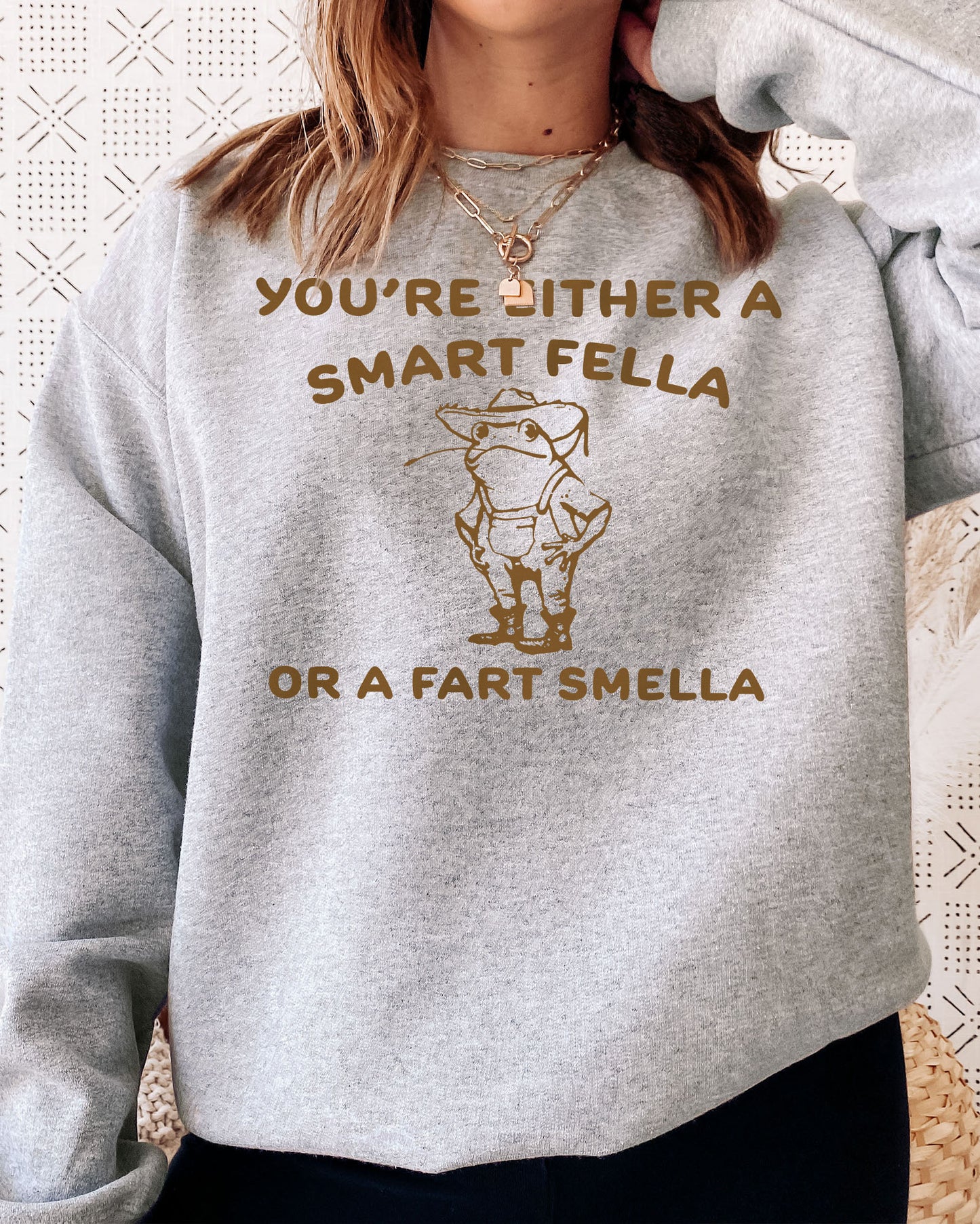 Woman wearing an ash gray sweatshirt featuring a funny retro country frog graphic and the quote 'You're Either A Smart Fella Or A Fart Smella'.