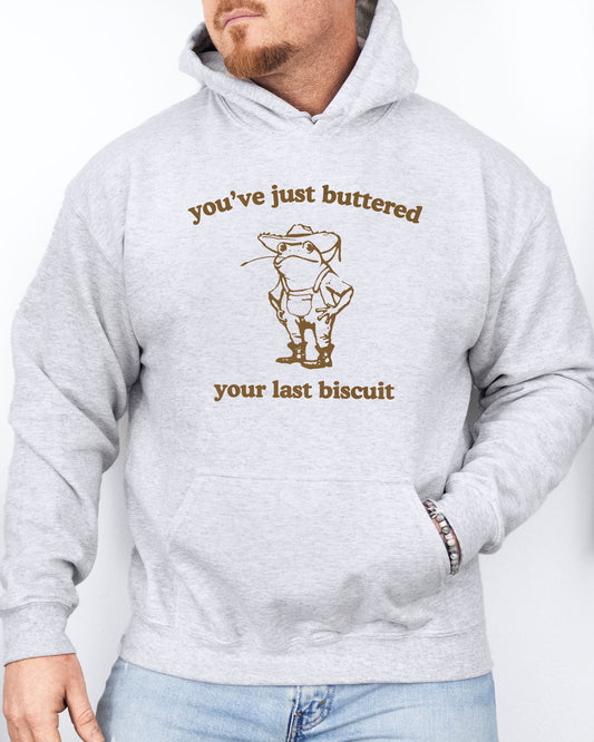 Man in a ash gray hoodie featuring a vintage country frog graphic with the quote 'You've Just Buttered Your Last Biscuit'.